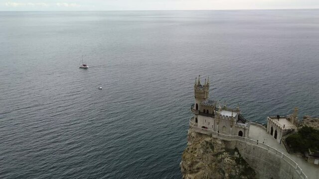 Departure of the drone from Swallow's nest in Crimea 4k video. The castle tower is on the edge of a high cliff. White yacht on the background of the Black Sea
