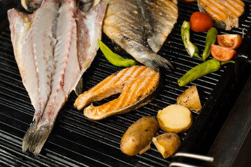 Cooking seafood mix of salmon, sea bass and vegetables. Grilling fish with chili potatoes and tomato.