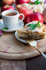 Apple homemade pie with red apples, mint and fork on wooden board on brown background. Rustic style