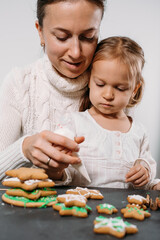 Obraz na płótnie Canvas Mother with child decorating gingerbread cookies with icing for Christmas. Homemade festive food. Cute toddler girl Family Workshop. Stars, tree