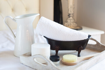 SPA and natural cosmetics theme. A jug, a white bath towel and jars of creams are on a wooden tray. Retro style.