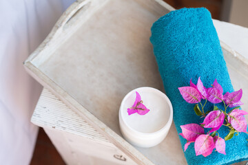 SPA and natural cosmetics theme. An aquamarine bath towel with a flower and a jar of cream are on a wooden tray. Copy space.