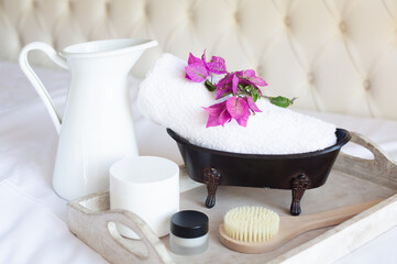 SPA and natural cosmetics theme. A jug, a white bath towel and some cosmetics are on a wooden tray on a white background. Retro style.