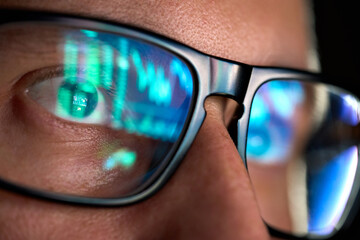 Focused crypto trader analyst wearing eyeglasses working looking at computer screen reflecting in...