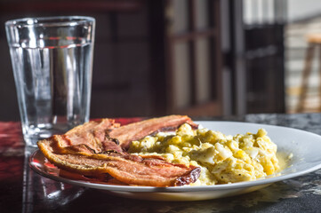sliced ​​bacon on a plate with scrambled eggs and a cup of coffee on the side