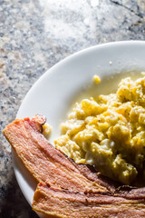 sliced ​​bacon on a plate with scrambled eggs and a cup of coffee on the side