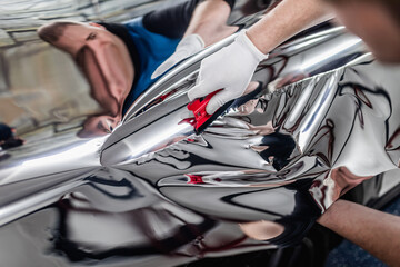 Car wrapping specialist putting silver mirror chrome foil on car. Selective focus.