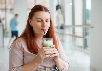 Happy Woman holding glass of healthy matcha tea. Girl drinking latte with straw at cafe table. Diet concept, copy space, web banner