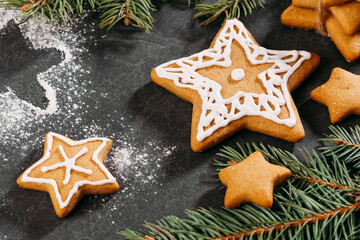 Christmas background with homemade star shape gingerbread cookies with icing on black table, copy space. Festive food, Post card, celebration traditions. pine tree brunch