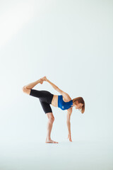 Athletic attractive woman in a top is training on a white background, doing leg stretches and looking down at the ground.