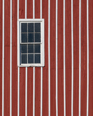 Window on red and white striped wooden barn exterior wall
