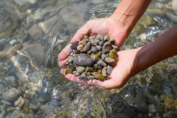 A lot of wet pebbles in female hands in sea water. Selective focus on the pebbles.