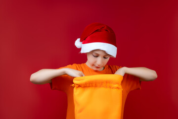 a boy with a Santa Claus Christmas hat opens yellow gift bags and looks in there