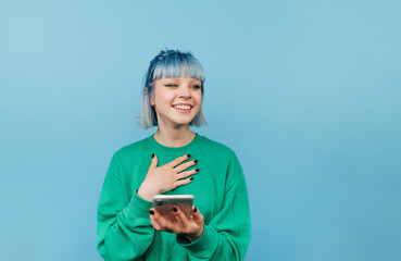 Happy girl with colored hair and makeup stands with a smartphone in his hands on a blue background...