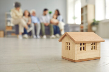 Close up of a small wooden house on the background of a large family who bought their own house....