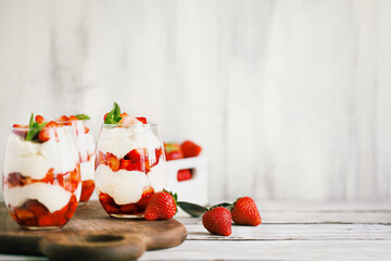 Healthy breakfast of strawberry parfaits made with fresh fruit, and yogurt over a rustic white table. Selective focus on glass in center. Blurred background and foreground.
