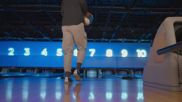 The camera follows one black man throwing a bowling ball on the playing track and jumping around rejoicing in the downed pins. One man bowling in slow motion