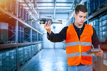 Warehouse worker launches drone. Young guy is holding quadcopter. Modern warehouse technologies. Using drone in warehouse business. Man is in oil depot. Barrels of oil stored on racks behind man.