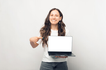 Fototapeta premium Cheerful young woman pointing at blank screen on laptop over white background.