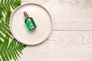 Natural cosmetics perfume essential oil serum in green glass bottle with dropper on plate, wooden background with green fern branches with copy space. eco ecology beauty concept.