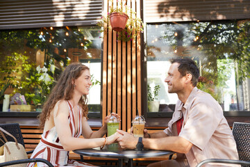 Side view portrait of happy couple holding hands at outdoor cafe while enjoying romantic date in Summer, copy space