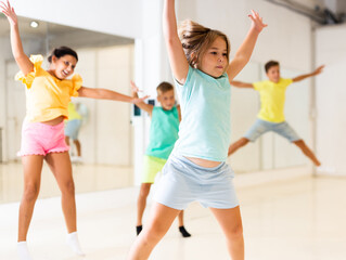 Happy cute sporty tween girl exercising in modern choreographic studio, jumping together with group of children.