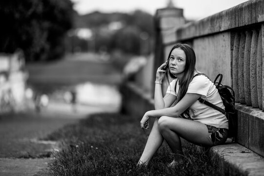 A girl talking on her cell phone while sitting in the park. Black and white photo.