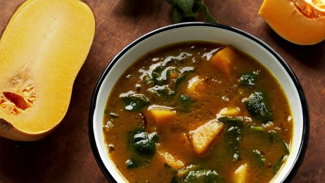 Hot soup from butternut squash and New Zealand spinach leaves in enamel bowl. Table spin.