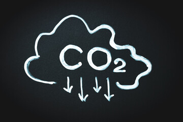 CO2 sign and arrows pointing down and cloud on black memo board. Reduce carbon dioxide emissions, limit global warming and climate change concept