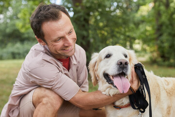 Portrait of happy man embracing dog outdoors in Summer at green park, copy space