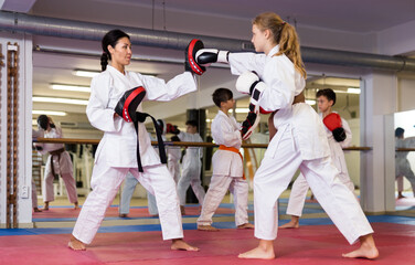 Young girls and boys in boxing gloves exercising jabs during group karate training. Trainer with...