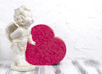Vintage baby angel figurine with heart shaped red gift box. Cupid statue on a white wooden...