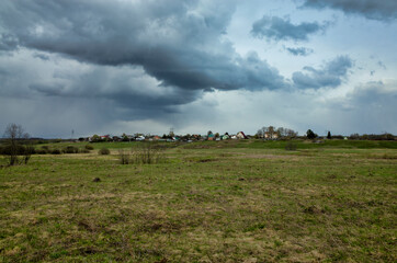 Obraz premium Spring meadow overlooking the village. The sky is covered with rain clouds. Nature of the Vladimir region, Russia