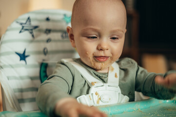 Baby eating with a face stained in food while in a child's dining chair