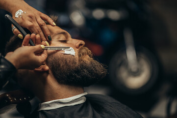 Man getting shaved with straight edge razor by hairdresser at barbershop