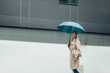 Businesswoman with umbrella walking down city street during rain