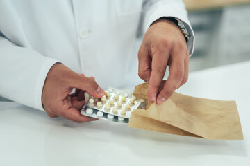 Hands of a pharmacist packing medications in a paper bag