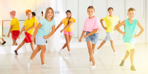 Group of cheerful tween children learning movements of vigorous dance in choreography lesson.