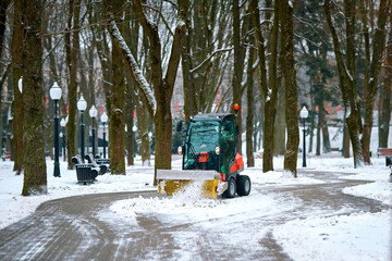 Tractor with rotating brush sweeping snow from footpath. Small tractor brushing snow from footpath,...
