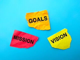 Colored wrinkled paper with word GOALS,MISSION,VISION on blue background.