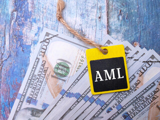 Banknotes and wooden board with text AML on wooden background.
