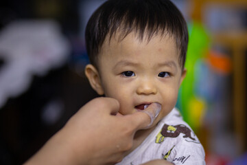 Close-up of mom hands clean the first teeth of her little baby son in the morning. Mother brushing teeth with a silicone fingertip toothbrush