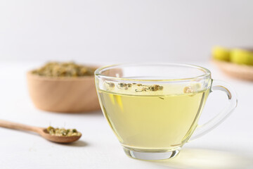 Chamomile tea in a cup glass with dried chamomile flowers in a spoon on white background, Healthy herbal tea