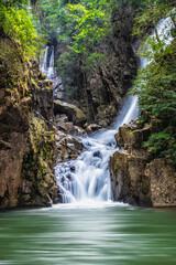 Fototapeta na wymiar waterfall over rock and green tree with green small lake