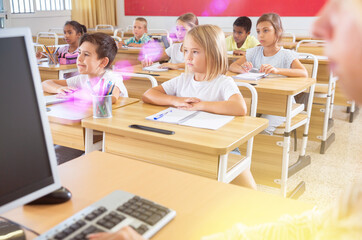 Fototapeta premium Group of preteen schoolchildren diligently working in class, making notes of teacher lecture
