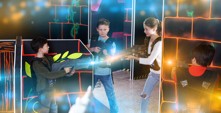 Modern teenage girl and boys with laser guns playing laser tag on dark arena
