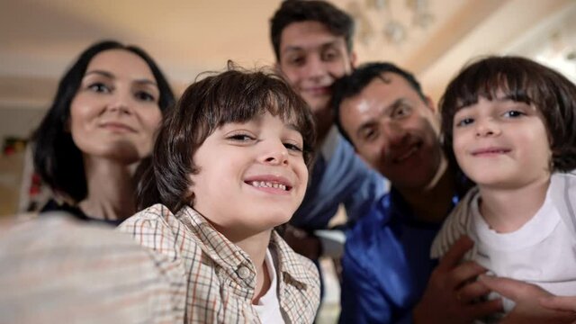 Cute little boy taking selfie with twin brother teenage brother father and mother on Christmas. Portrait of smiling happy Middle Eastern kid enjoying New Year celebration at home indoors