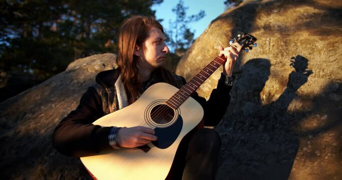 Man playing guitar in the forest on the sunset. Guy plays guitar in the mountains, close up view. Entertainment, travelling concept.