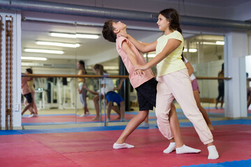 Diligent positive schoolchilds boy and girl practicing karate kicks in pairs in gym