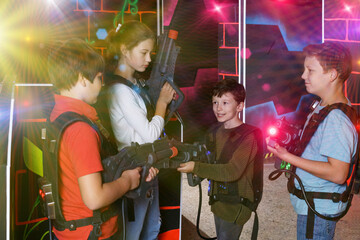 Jolly teens aiming laser guns at other players during lasertag game in dark room